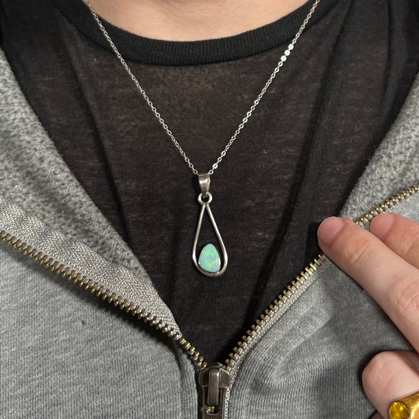 Person wearing a gray hoodie with a black shirt underneath, focusing on a silver necklace with a green opal pendant.
