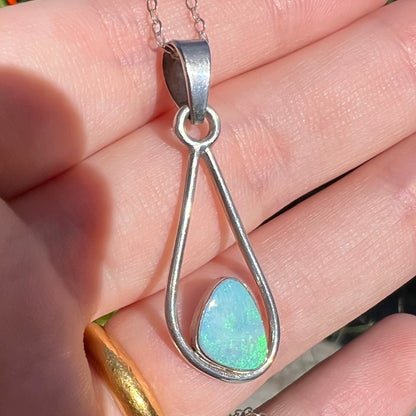 Sterling silver opal pendant with green play of color held in a hand in natural sunlight.