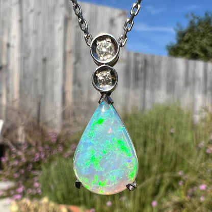A platinum drop pendant mounted with two diamond accents and a pear shaped green-blue crystal opal.