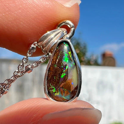 A pear shaped boulder opal necklace in sterling silver.  The opal has bright green and blue flashes.