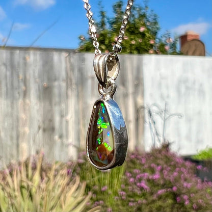 A pear shaped boulder opal necklace in sterling silver.  The opal has bright green and blue flashes.