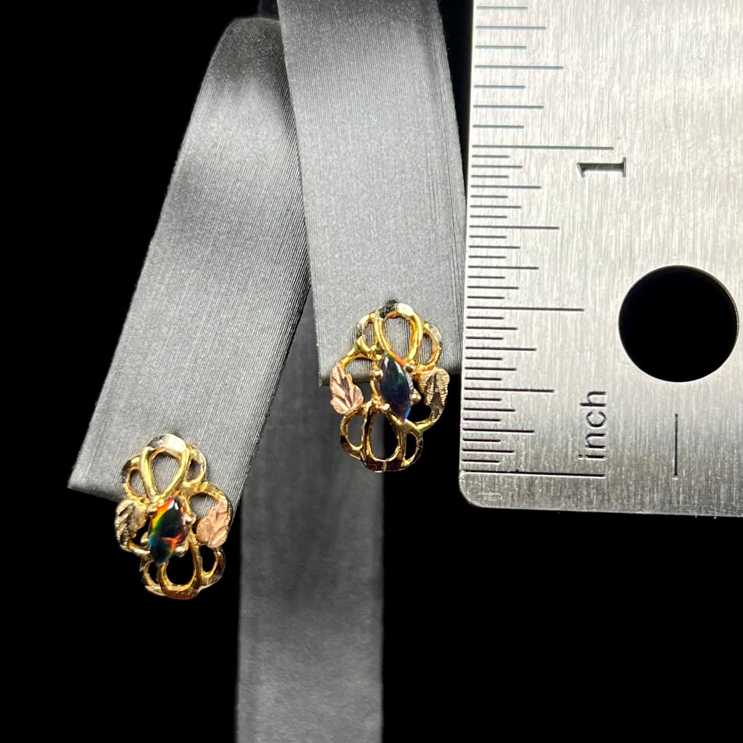 Half inch-long Black Hills gold marquise opal earrings on display next to ruler