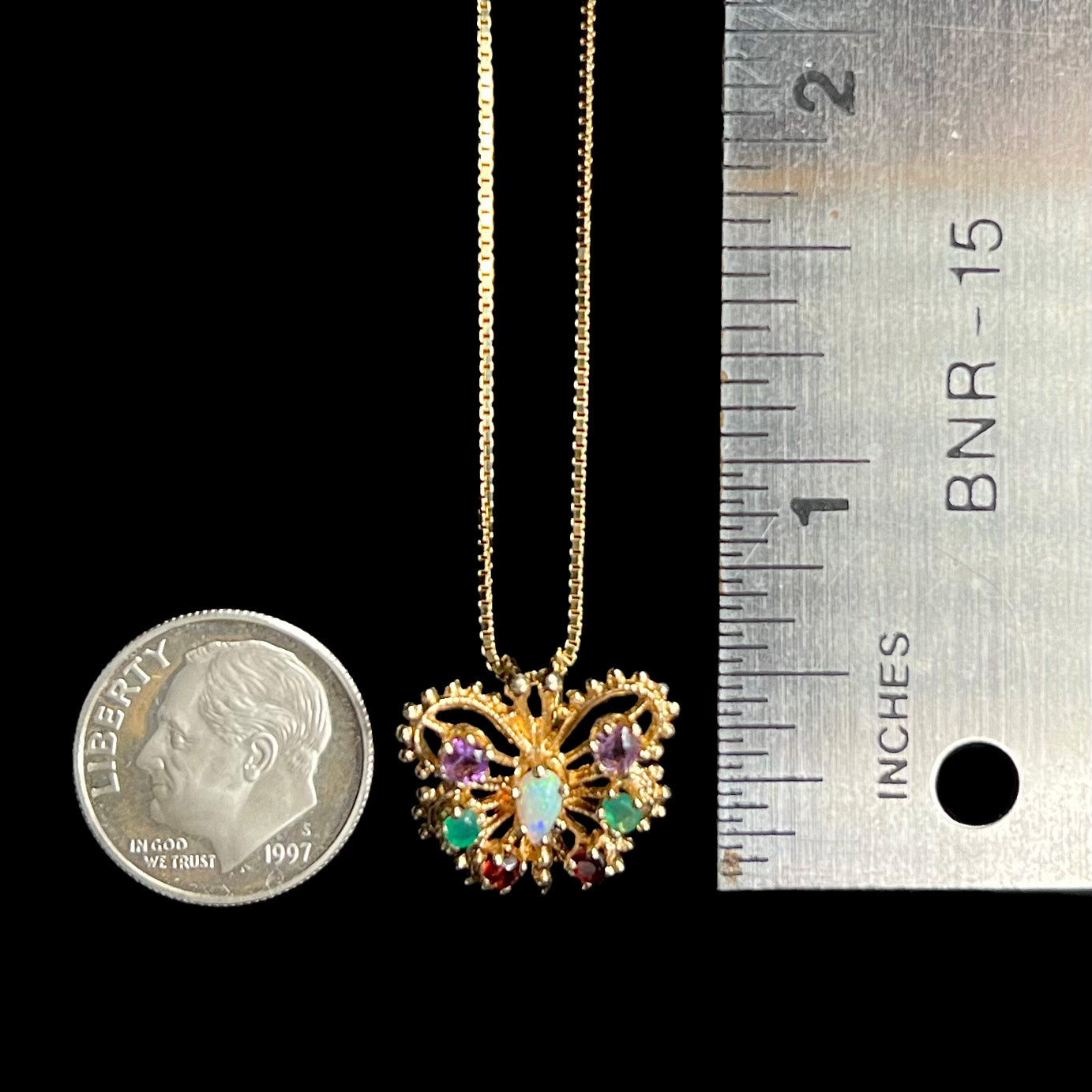 A half-inch long 14k gold multi-gemstone butterfly pendant on chain next to US dime coin and ruler for scale.