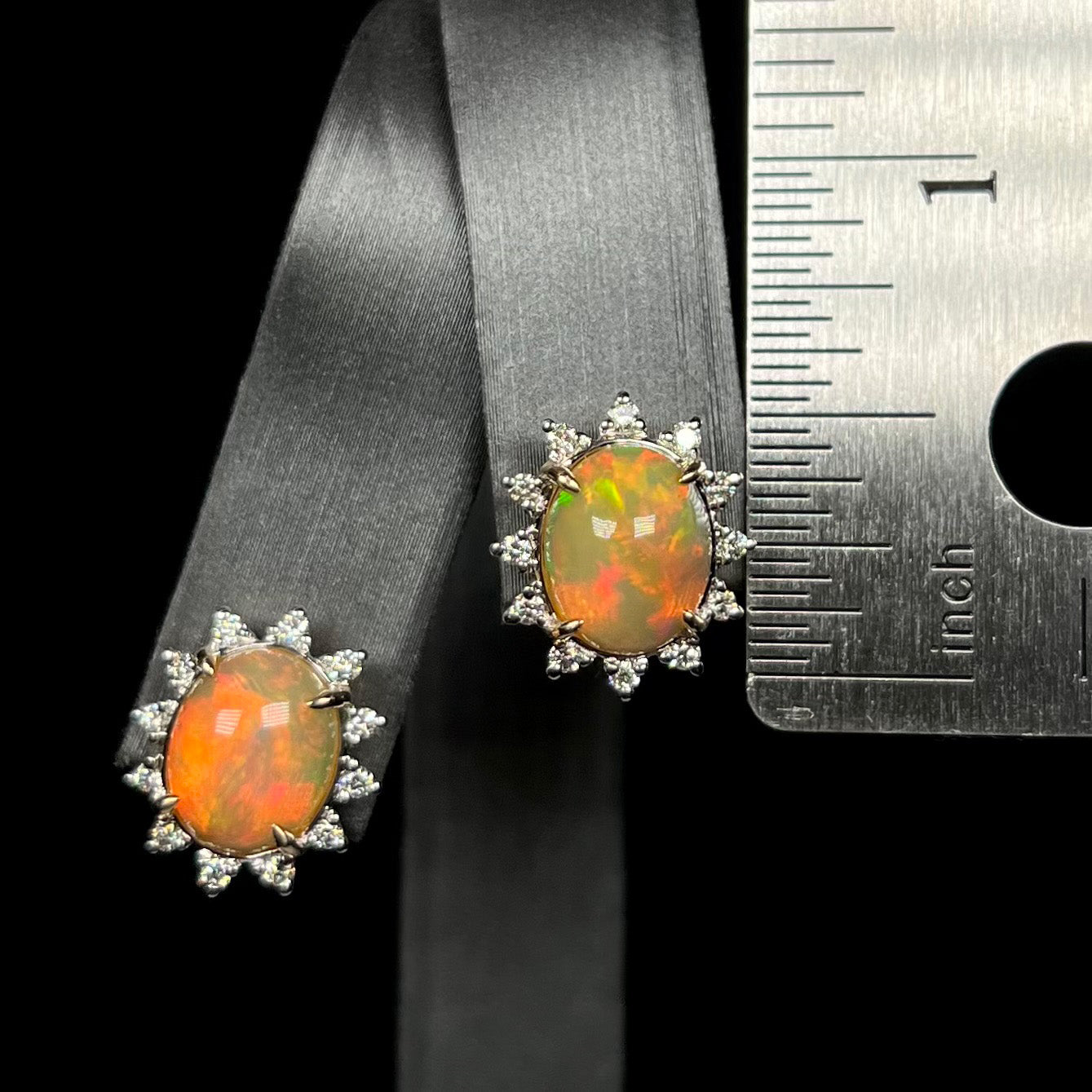 Half inch-long Ethiopian opal and diamond halo stud earrings on earring display next to ruler