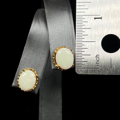 Half inch-long oval shaped opal stud earrings on earring display next to ruler