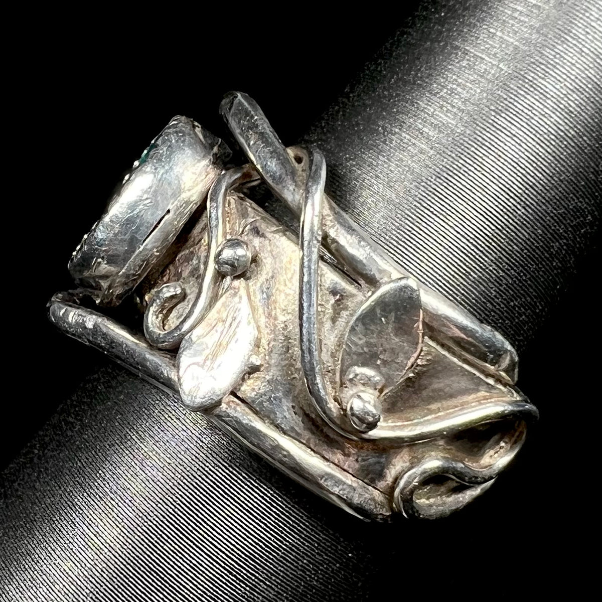 Side view of handcrafted sterling silver ring featuring wrapping vine and leaf design along ring's shank, viewed on display