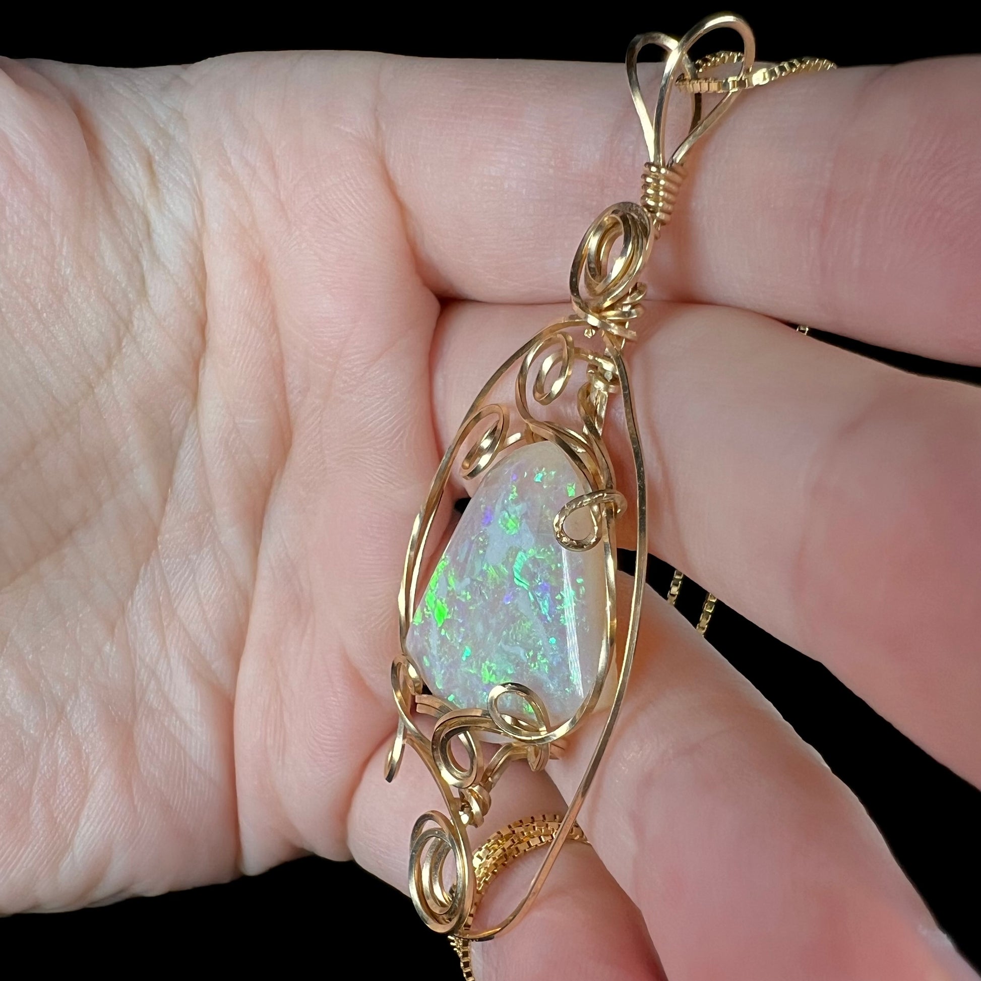 An Australian opal solitaire pendant featuring a handmade, Boho-inspired wire wrapped design, shown close-up from a side angle in a hand.