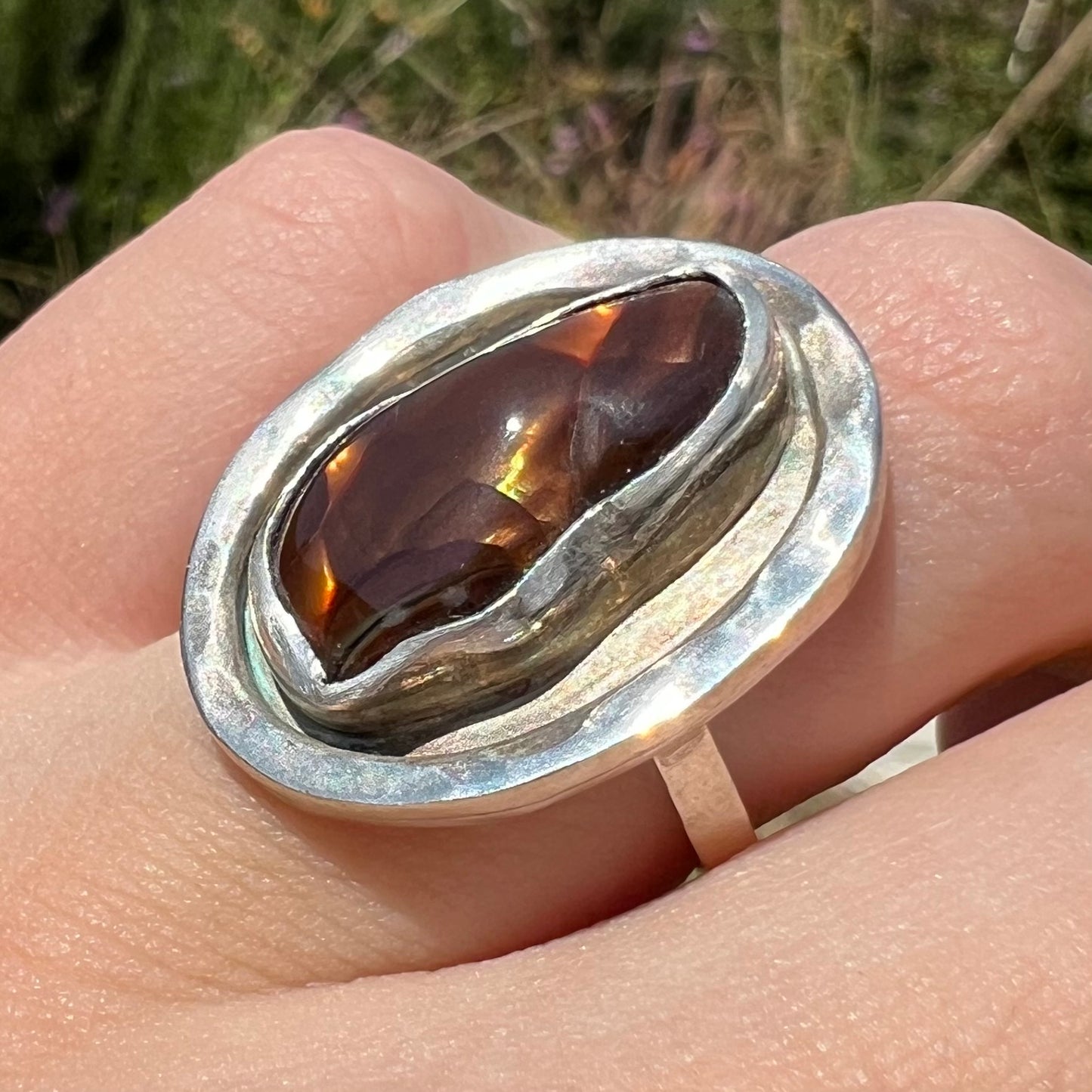 Anlged close-up of a handmade sterling silver fire agate ring worn in sunlight on a finger.