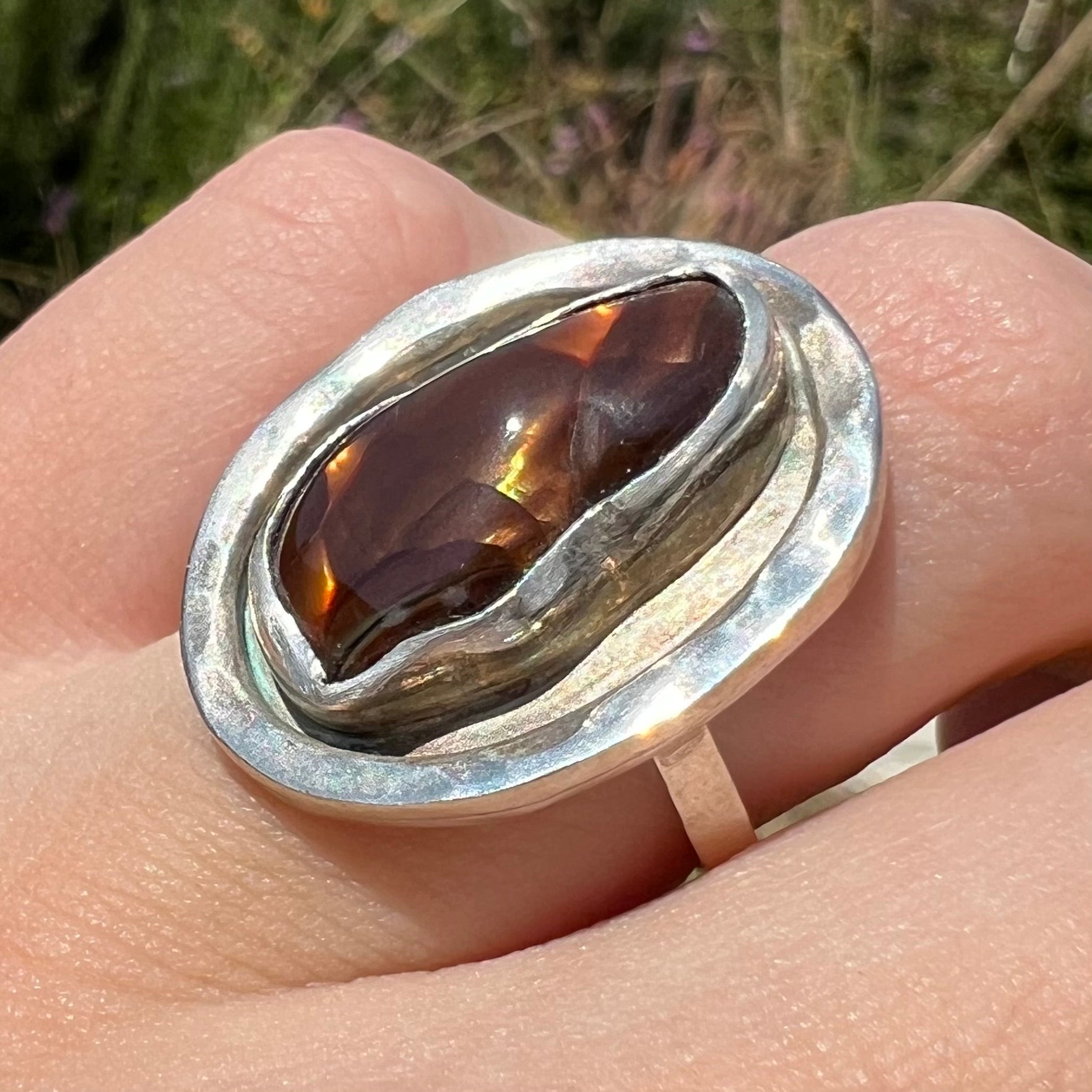 Anlged close-up of a handmade sterling silver fire agate ring worn in sunlight on a finger.