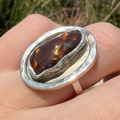 Anlged close-up of a handmade sterling silver fire agate ring worn in sunlight on a finger.