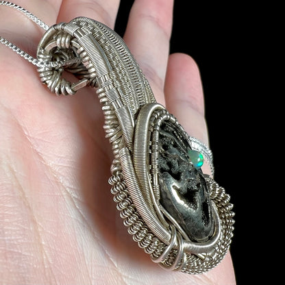 Side view of a handmade silver wire wrapped ammonite and opal-accented pendant, held in a hand.