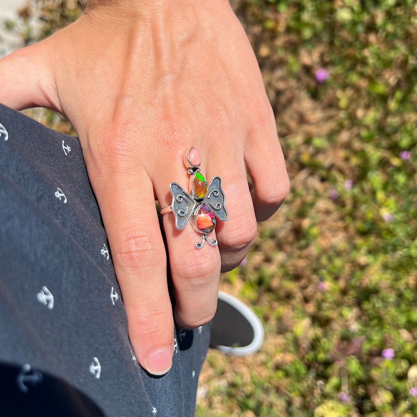 A handmade opal butterfly ring worn on a hand as it rests on the model's hip.