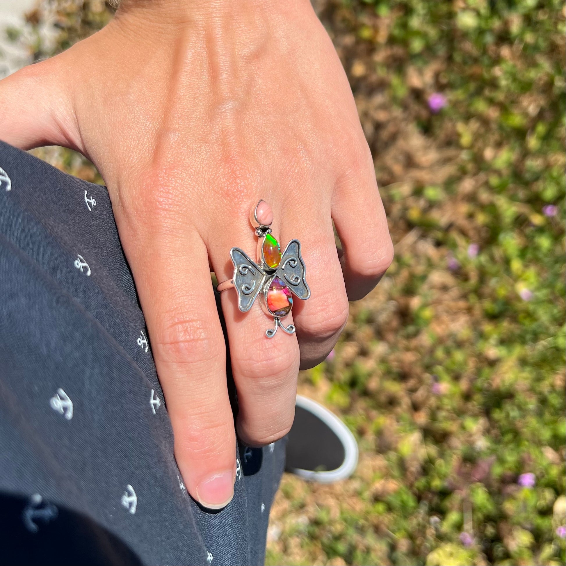 A handmade opal butterfly ring worn on a hand as it rests on the model's hip.