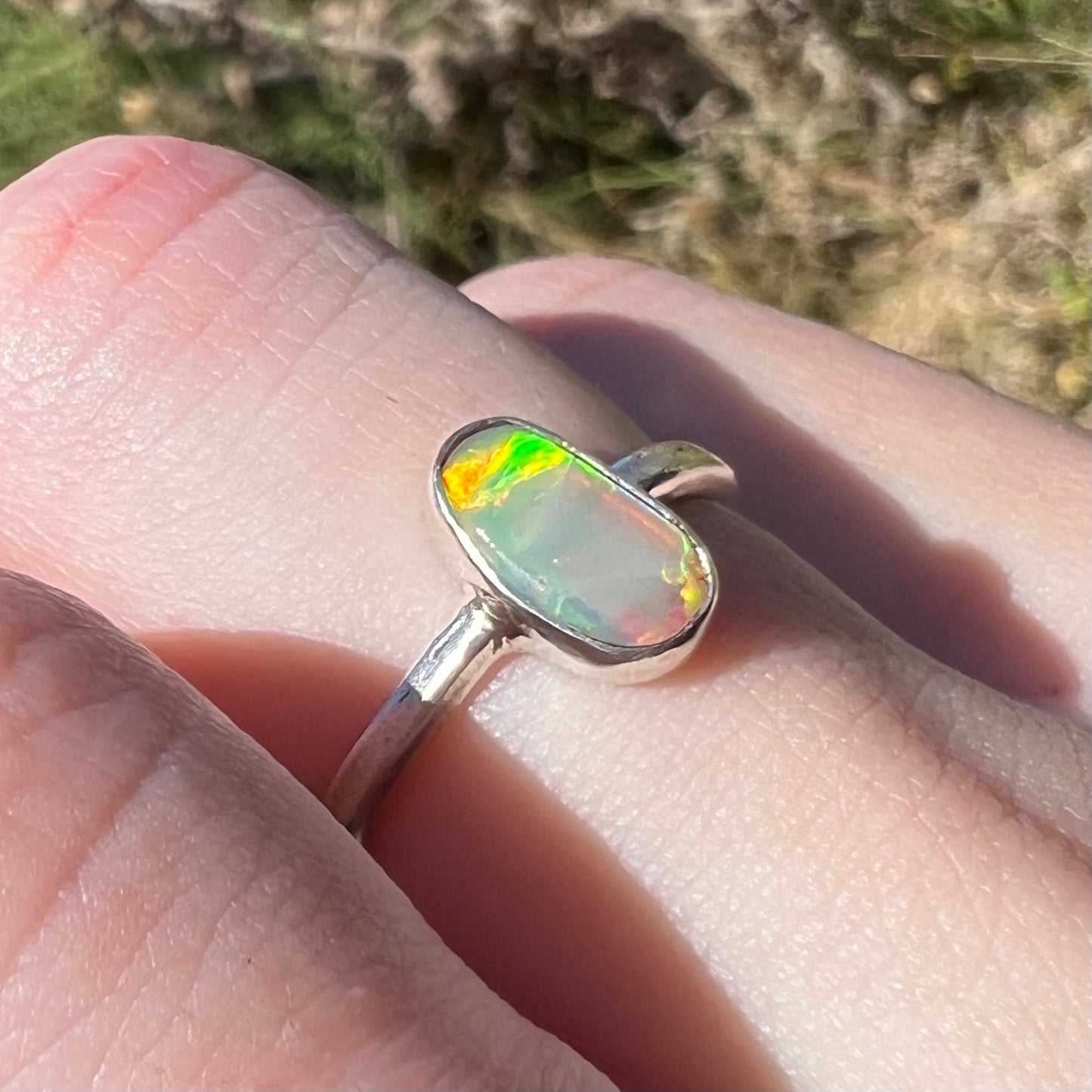 Angled view of a handmade sterling silver Australian crystal opal ring, viewed in the sunlight.  The opal has green and orange flashes around one edge.