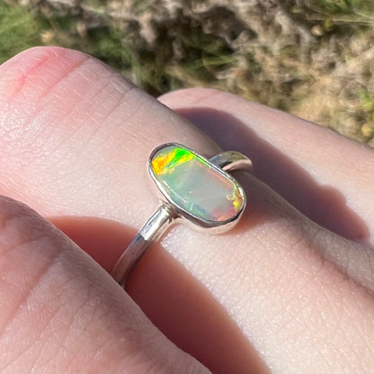 Angled view of a handmade sterling silver Australian crystal opal ring, viewed in the sunlight.  The opal has green and orange flashes around one edge.