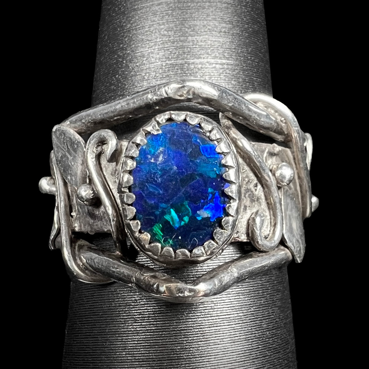 Close-up of sterling silver black opal doublet ring with nature-inspired leaf and vine design on ring display, handmade by artist Hailey Johnson