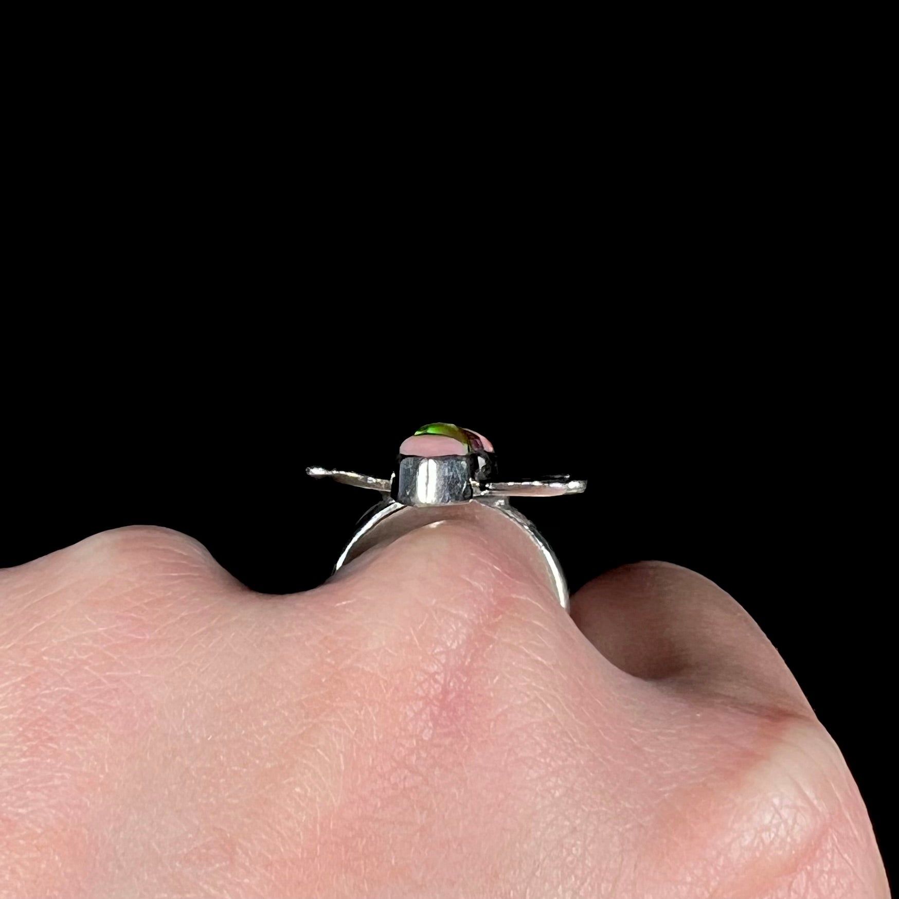 The side gallery profile view of a handmade silver butterfly ring shown on a hand.