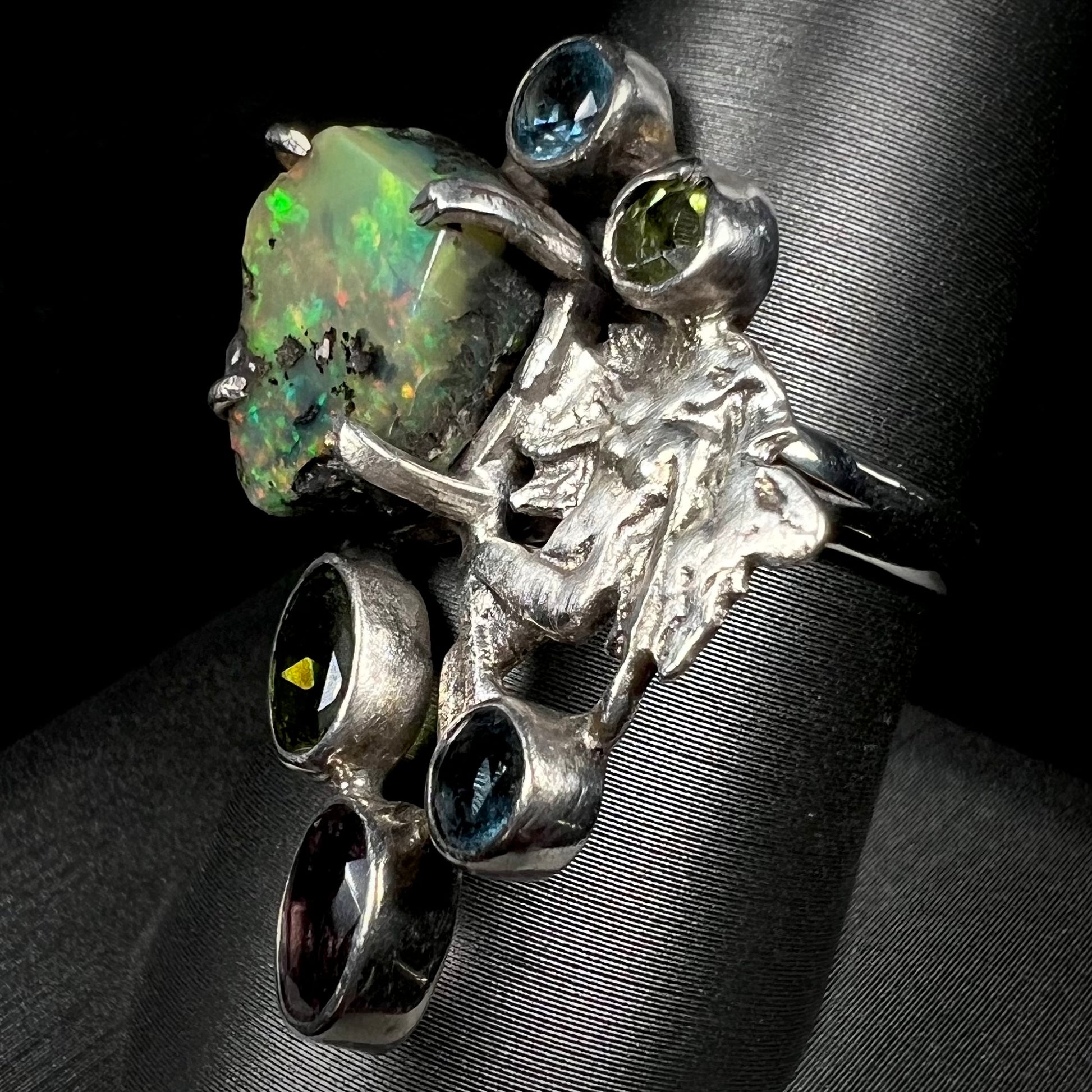 Angled view of a silver men's ring set with rough Virgin Valley opal and gems with a female figure design.