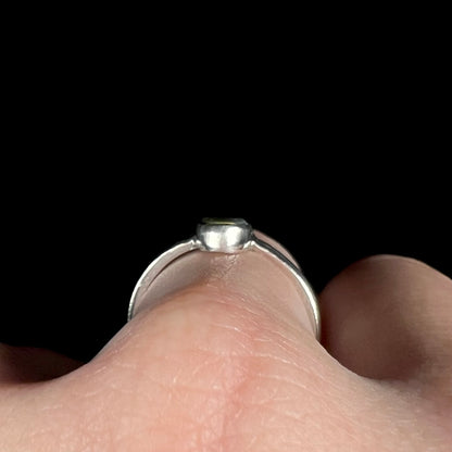 Side gallery profile view of a handmade sterling silver opal ring worn on a hand against a black backdrop; the top of the opal is barely visible.