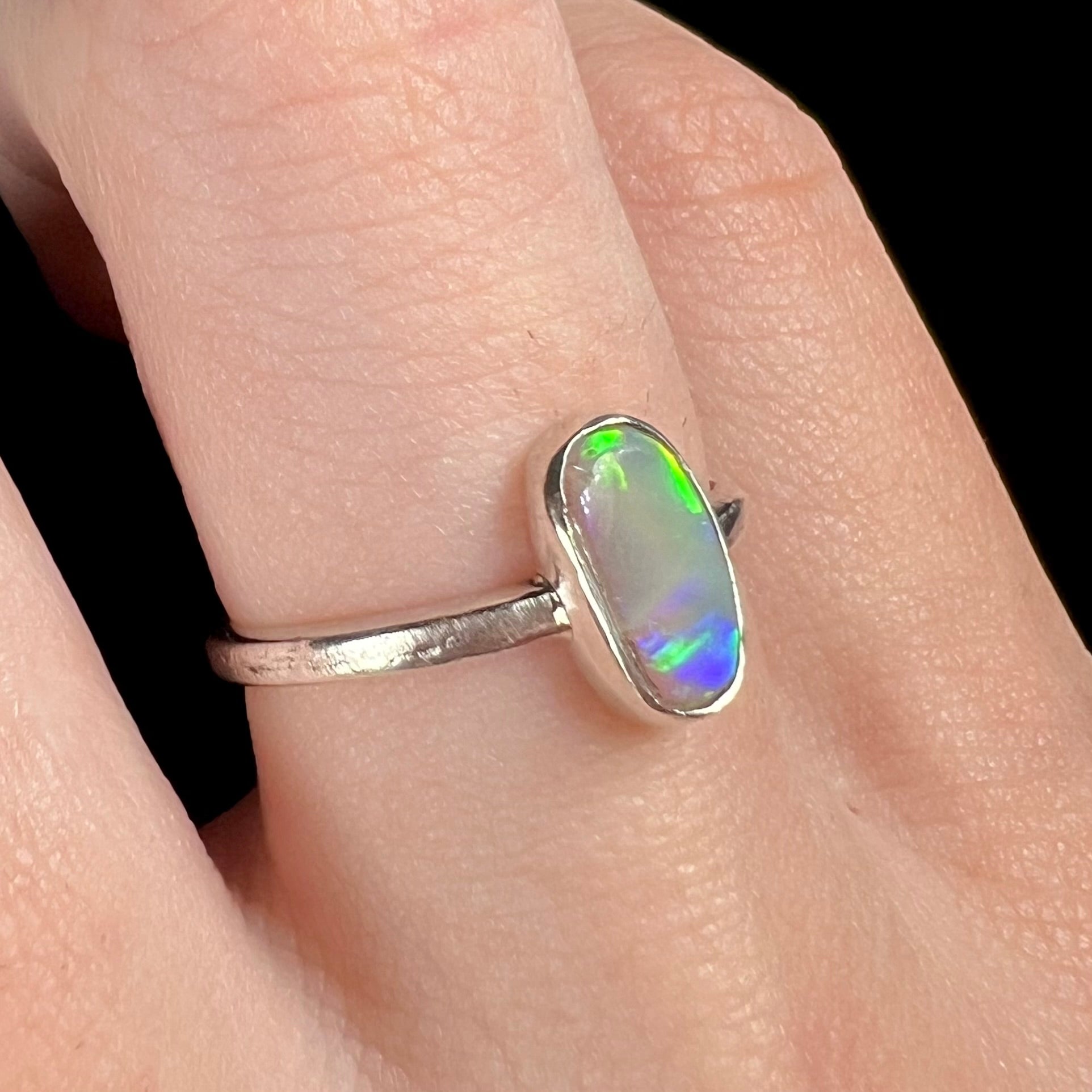 A handmade, freeform-shaped Australian crystal opal women's ring shown close-up on a finger under studio LED light.