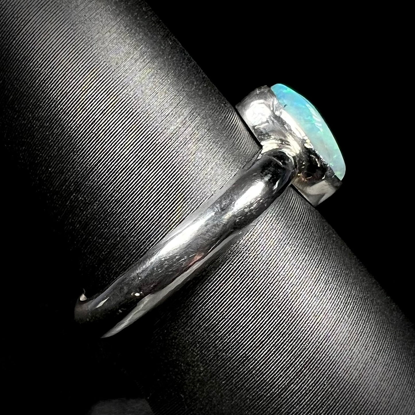 Side close-up view of a handmade sterling silver Australian opal ring on a ring display.  The shank is in focus, and tooling marks can be seen.