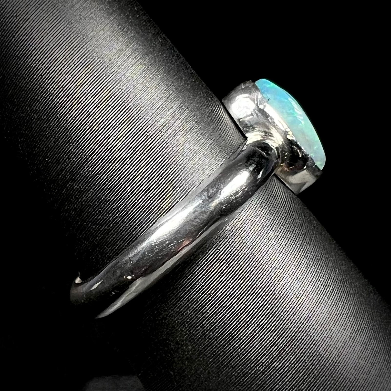 Side close-up view of a handmade sterling silver Australian opal ring on a ring display.  The shank is in focus, and tooling marks can be seen.