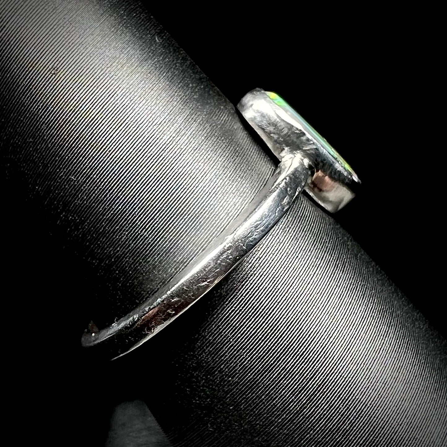 Side view of a handmade sterling silver opal ring on a ring display. The ring's shank and bezel setting show tooling marks.