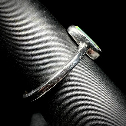 Side view of a handmade sterling silver opal ring on a ring display. The ring's shank and bezel setting show tooling marks.