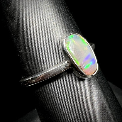 Angled close-up of a handmade sterling silver opal solitaire ring on a ring display.  The opal has purple and green play of color.