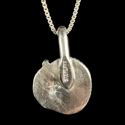 Back side of a sterling silver pendant necklace featuring a textured, organic circular disc with a bail, shown on a black background. The word 'STERLING' is engraved on the back of the bail; a letter "J" might also be seen