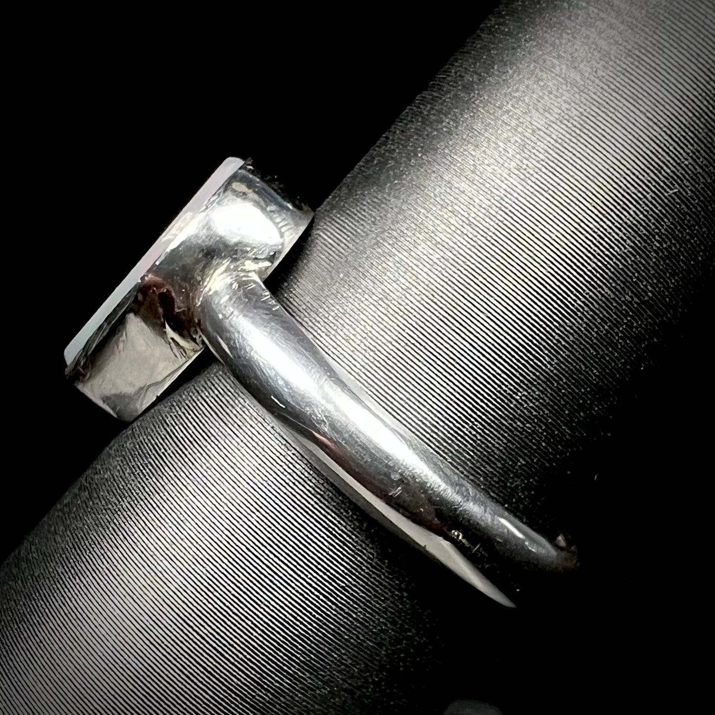 Side shank view of a handmade sterling silver solitaire opal ring on a ring display.  The shank and opal's bezel setting are in view.