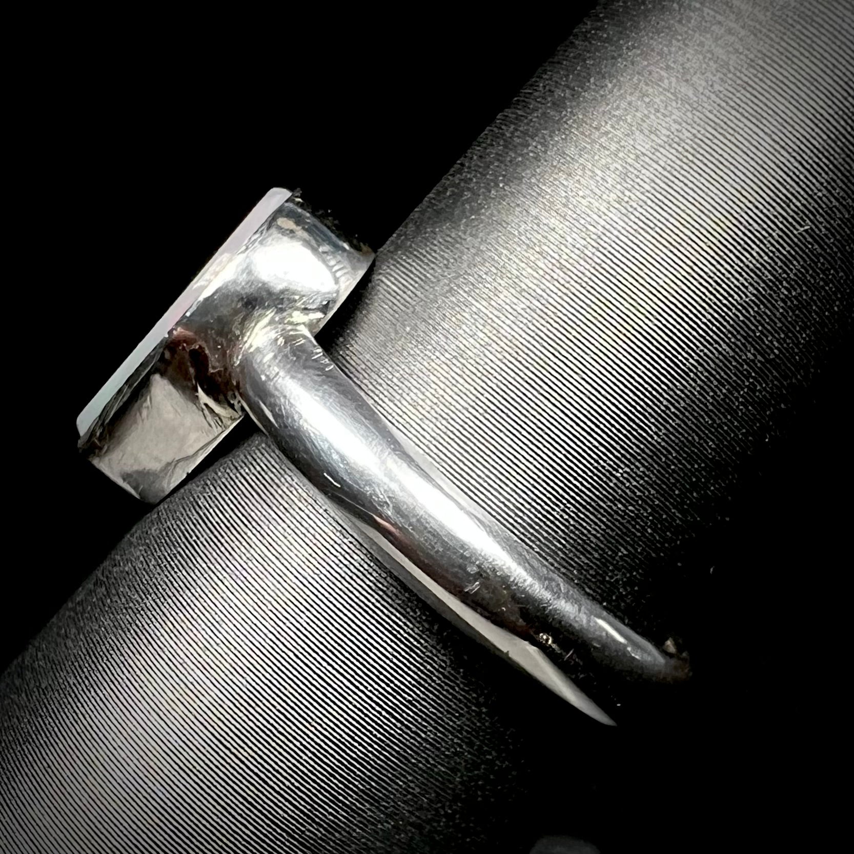 Side shank view of a handmade sterling silver solitaire opal ring on a ring display.  The shank and opal's bezel setting are in view.
