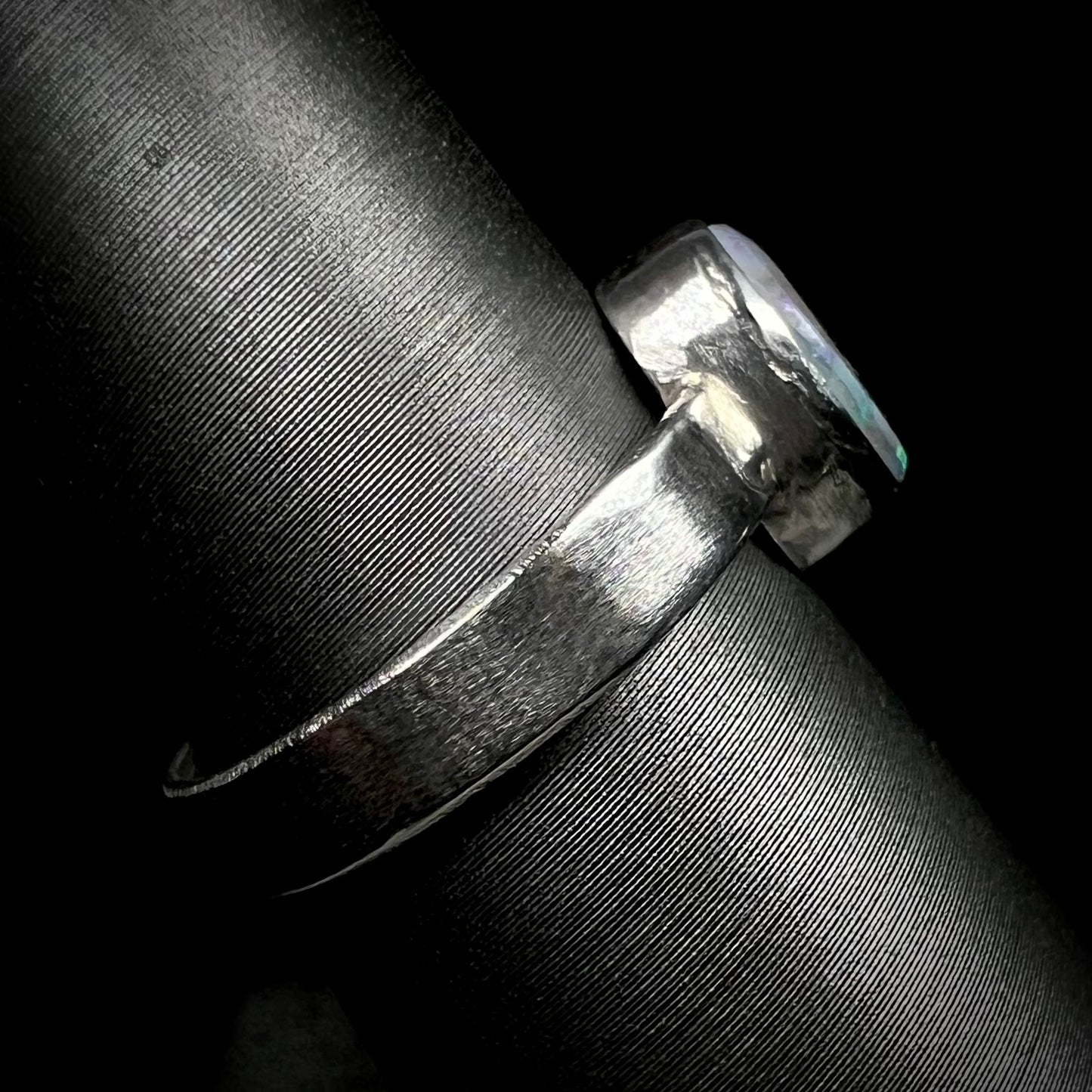 Side view of a unisex opal ring on a ring display.  The handmade sterling silver shank is in focus.