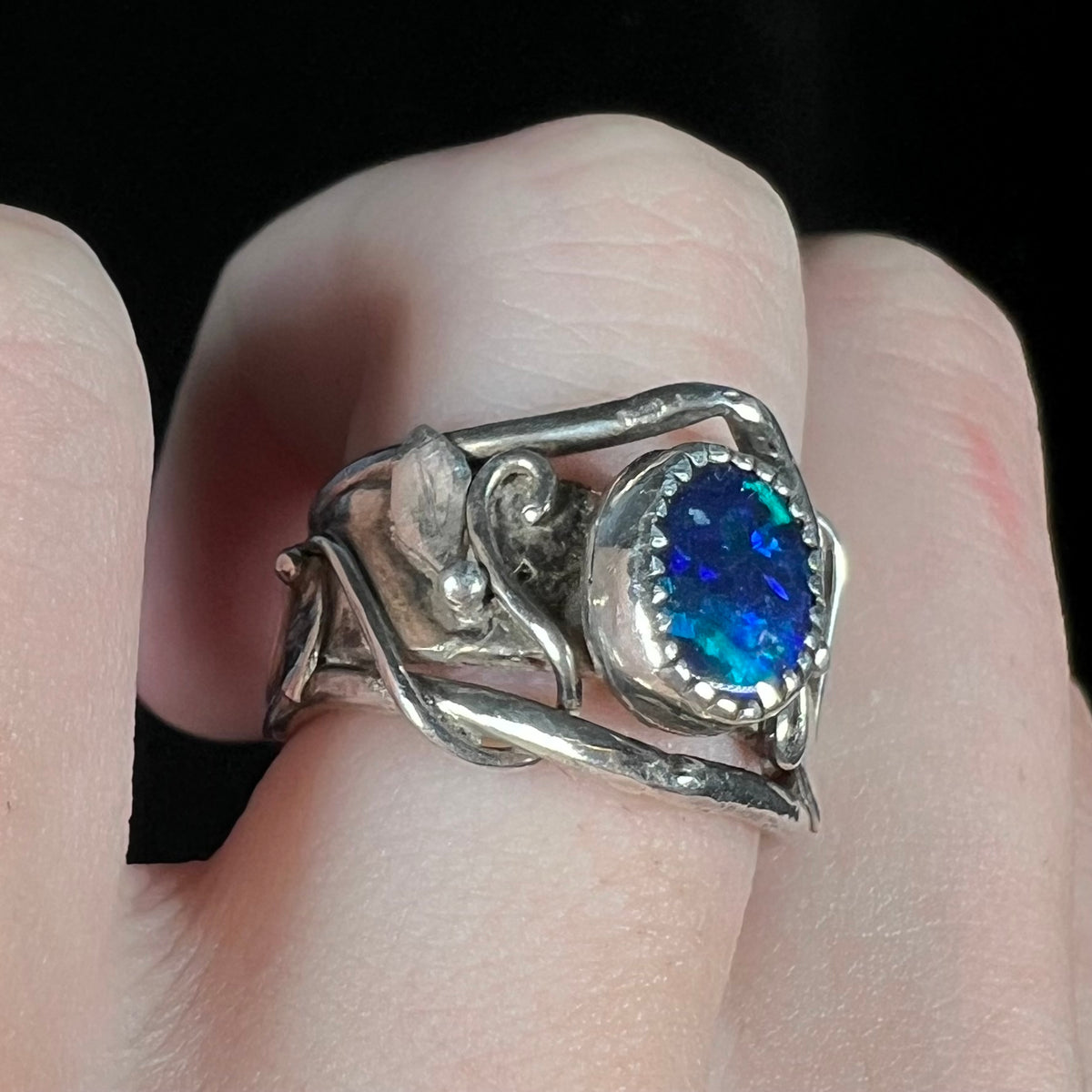 Close-up of finger wearing handmade sterling silver black opal doublet ring with twisting leaf and vine design