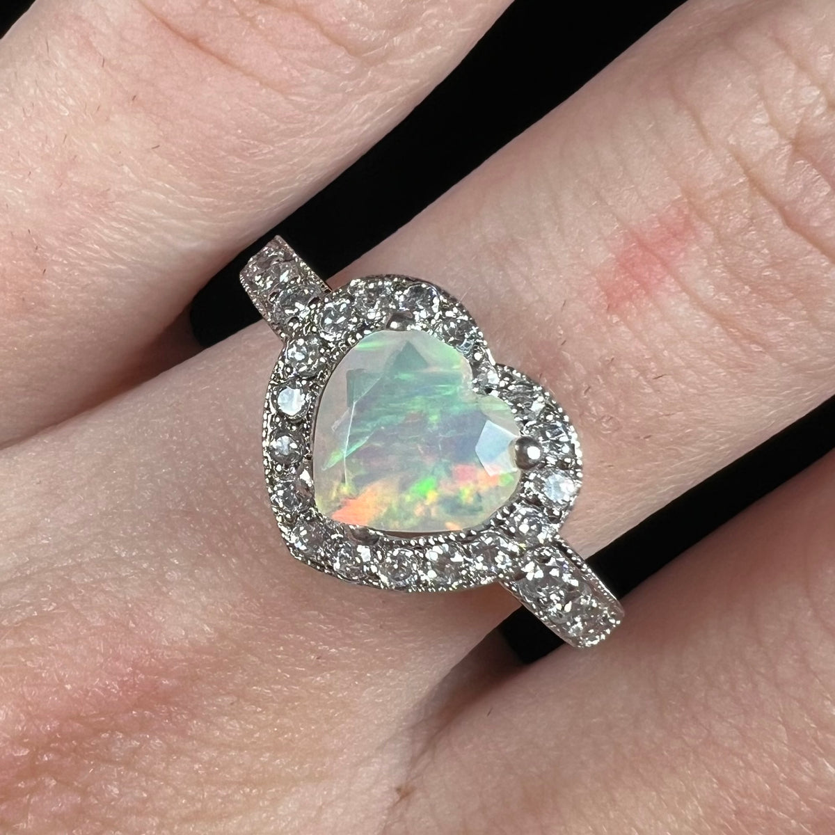 Close-up of heart cut Ethiopian opal ring with CZ halo design, worn on finger