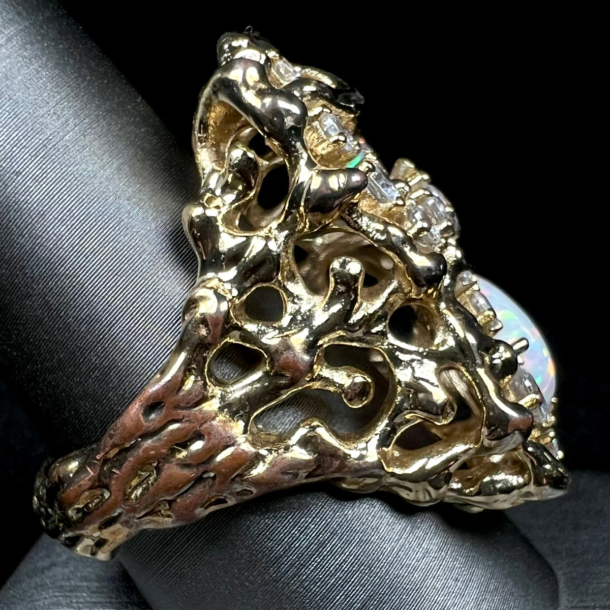 A heavily-weighted gold-plated opal and CZ men's ring shown from side view on ring display, the gold plating worn along the ring's shank exposing the copper alloy underneath.