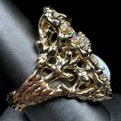 A heavily-weighted gold-plated opal and CZ men's ring shown from side view on ring display, the gold plating worn along the ring's shank exposing the copper alloy underneath.