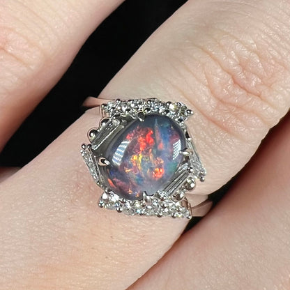 Close-up of N5 dark opal ring featuring hexagonal halo design set with round and tapered baguette cut diamonds, worn on finger.