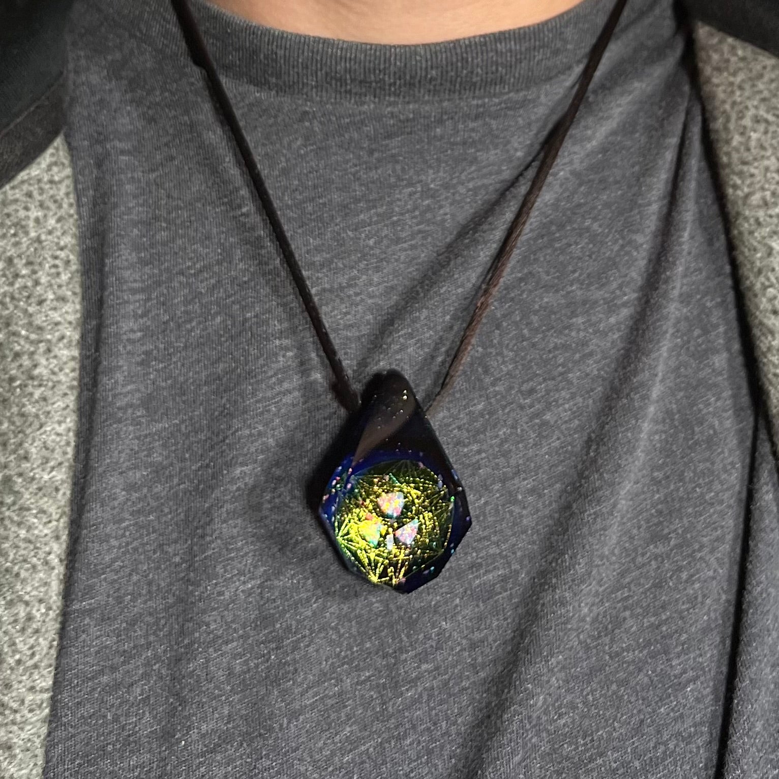 Close-up of an opal in glass necklace with a hexagram star design, worn around a person's neck against dark shirt.
