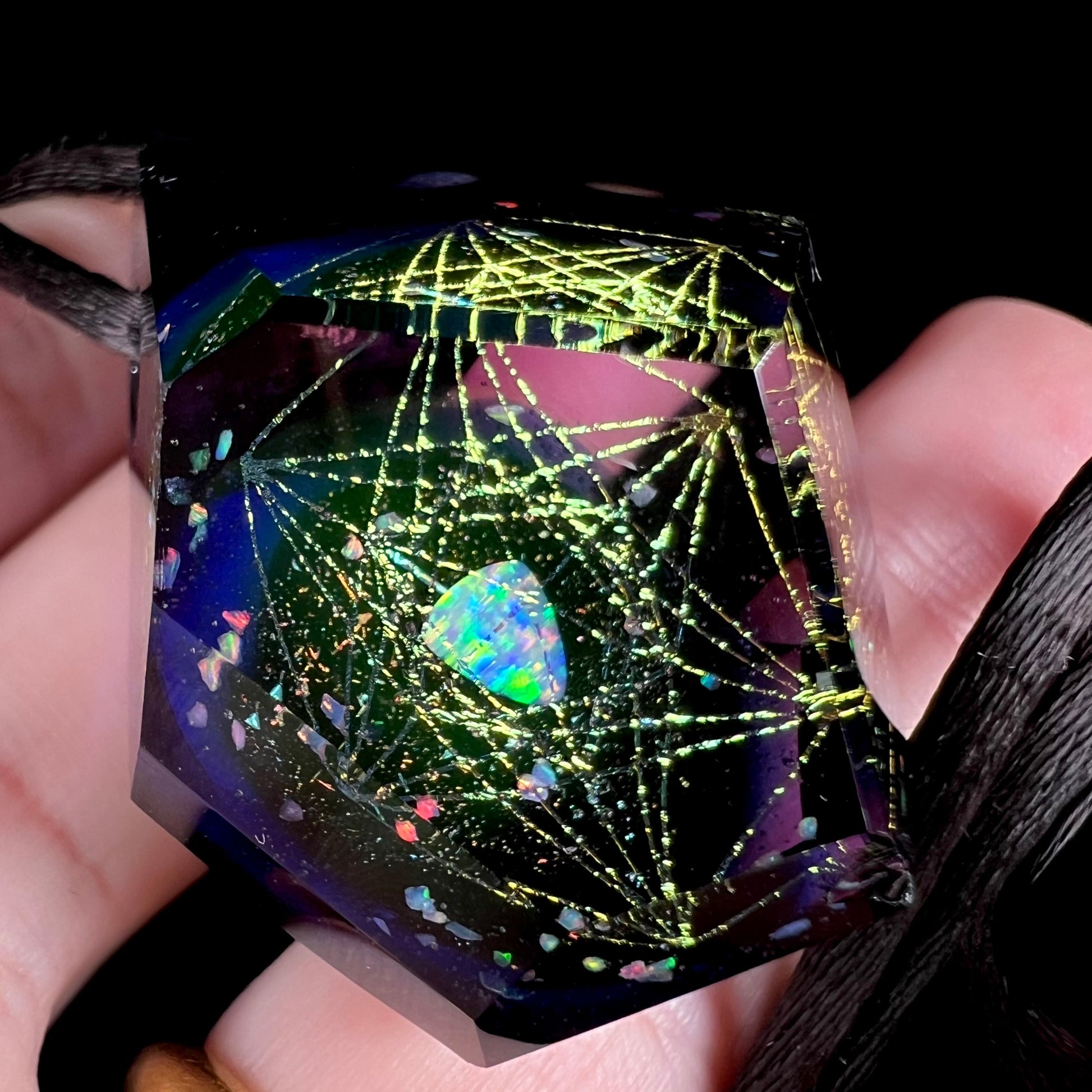 Close-up of a hexagram design in a purple glass and lab opal pendant, shown from an angle in a hand against a dark background.