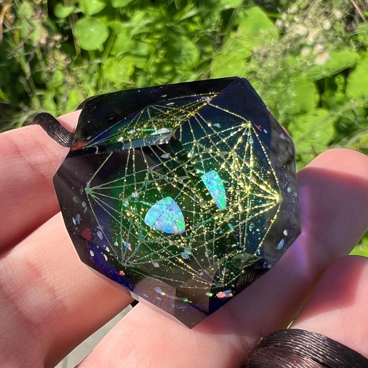 Underside of a faceted glass pendant featuring a hexagram star design, shown in the sunlight against a blurred green background.