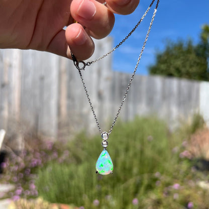 A platinum drop pendant mounted with two diamond accents and a pear shaped green-blue crystal opal.