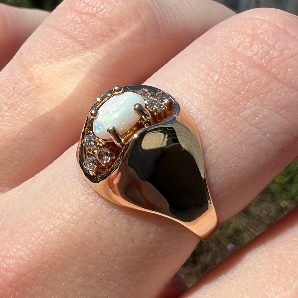 High, reflective polish is notable across 14k yellow gold surface of Mid-Century opal and diamond ring, worn on finger and viewed from angle in sunlight