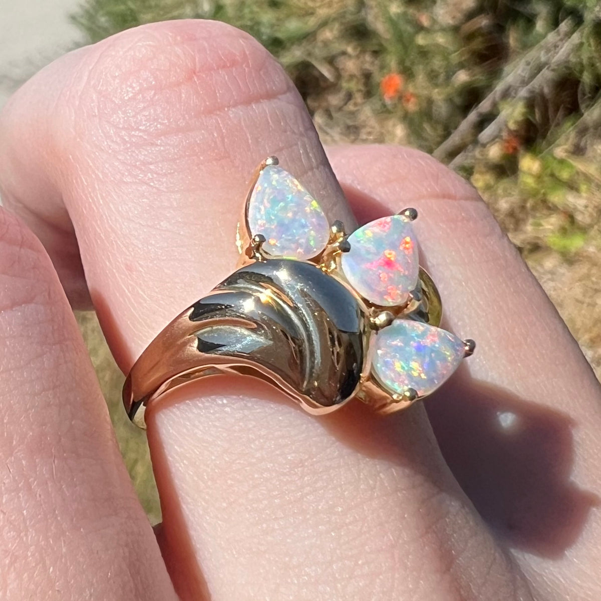 Yellow gold Australian crystal opal ring worn on finger, shown from angle in natural light; a high-polish domed Modernist design detail is in focus.