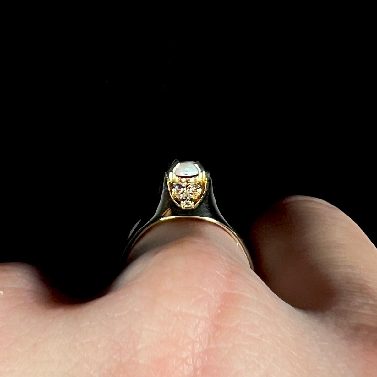 Side profile gallery view of a Mid-Century style 14k gold opal and diamond ring, worn on a hand; the ring has a high-profile domed design, three round diamonds and the edge of the opal in view