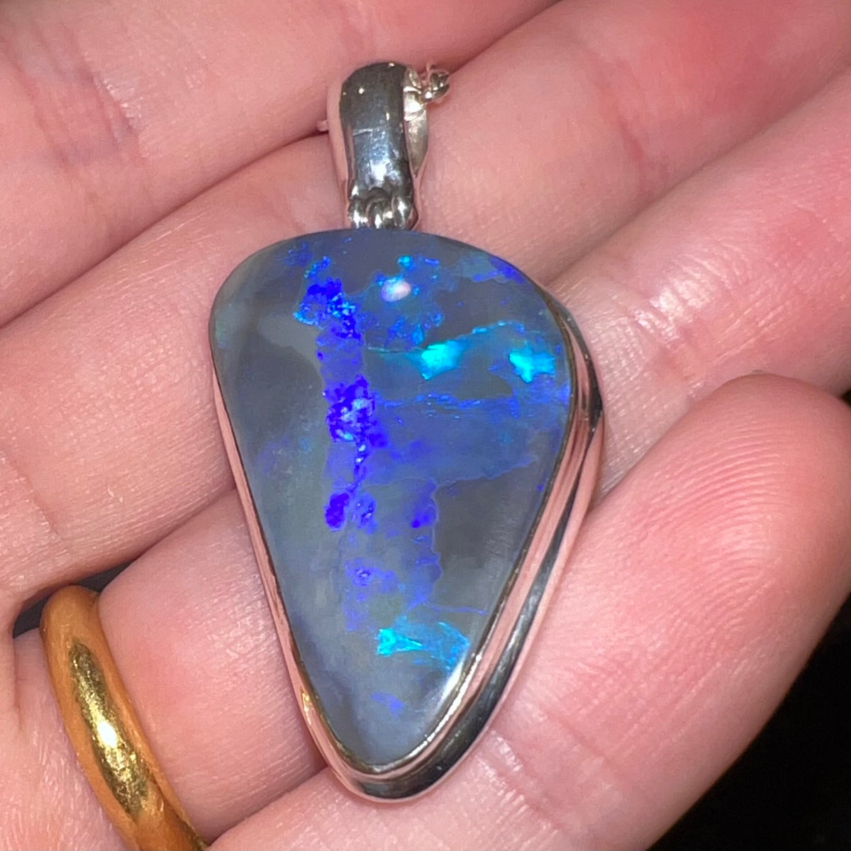 Highly-directional blue play-of-color seen in silver black opal pendant, held in hand, viewed from bottom-side-up with camera flash