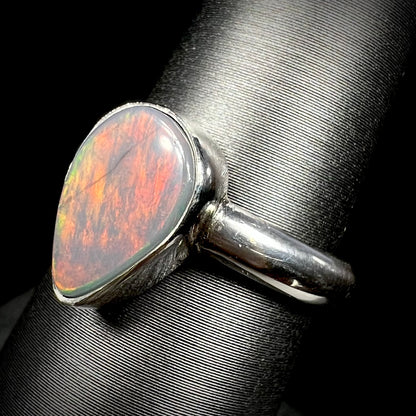 Angled close-up of a natural dark opal ring in sterling silver with highly reddish, orange, and green flashes of color, shown on a ring display.