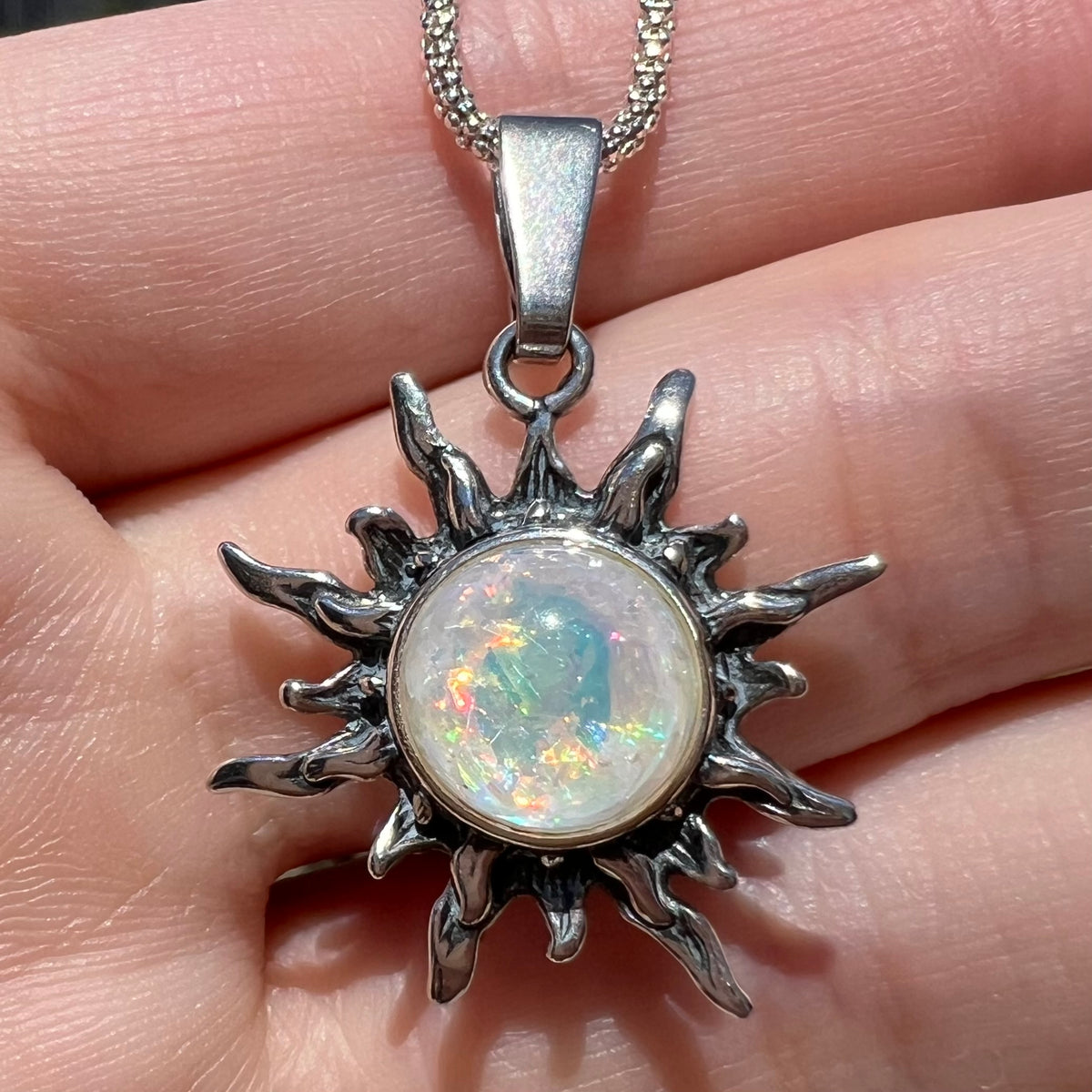 Close-up of an imitation foil-in-glass opal sunburst pendant in sterling silver, held in a hand in sunlight.