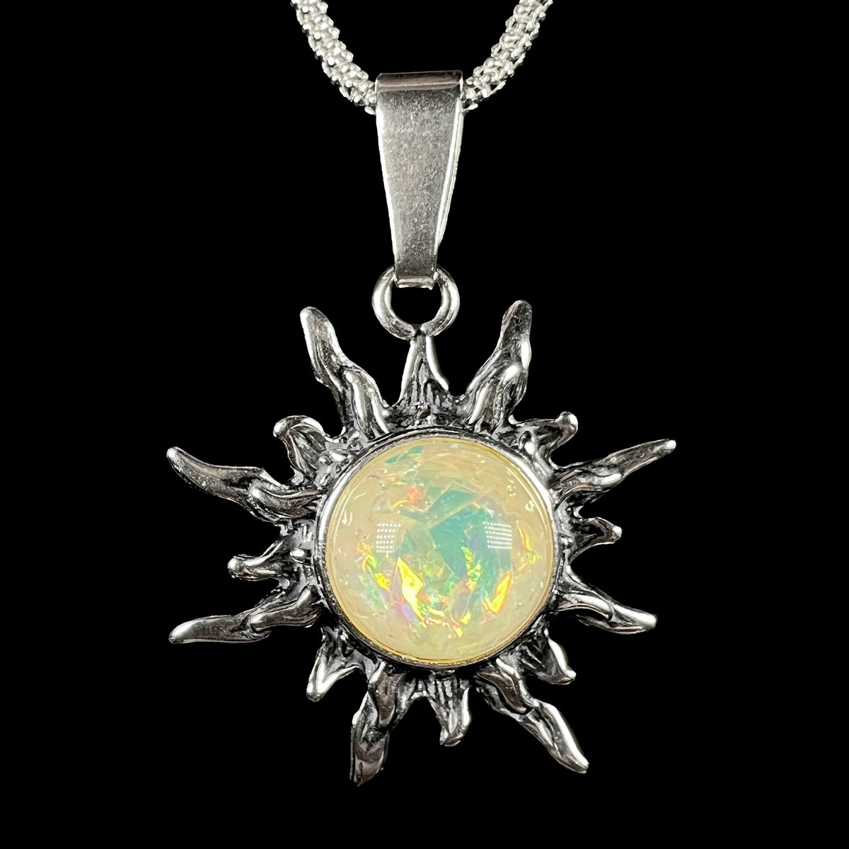 Front close-up of a sterling silver sun pendant mounted with a round, pale yellowish imitation opal, shown on a chain against black background.