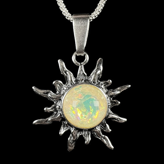Front close-up of a sterling silver sun pendant mounted with a round, pale yellowish imitation opal, shown on a chain against black background.